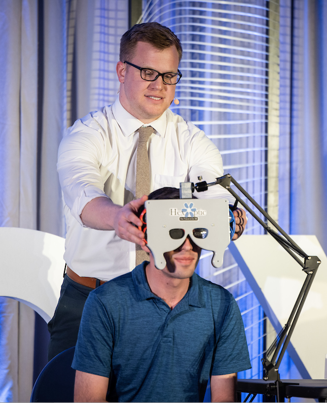 A student places an eye exam tool on a seated person.